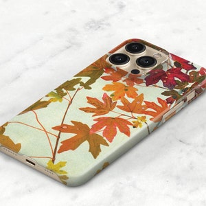 May include: A smartphone case featuring a light cream background with a pattern of autumn maple leaves in shades of orange, red, yellow, and brown. The case has a cutout for a triple-lens camera system and visible side buttons on the right edge.