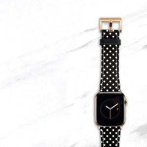 May include: A black and white polka dot watch band with a gold watch face. The watch face has a black background and white hands.