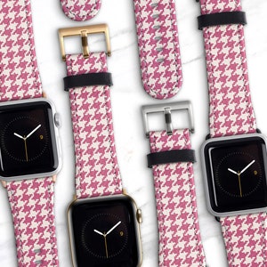 May include: Several smartwatches with pink and white houndstooth patterned bands are displayed. The watch faces are black with white hands. The bands have black leather backing and silver or gold buckles. The watches are on a white marble surface.