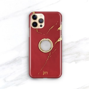 May include: Red phone case with a gold marble pattern and a gold ring holder. The case has the letters "jm" printed on the bottom.