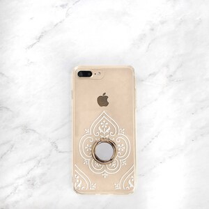 May include: A gold iPhone case with a white intricate design and a gold ring holder.