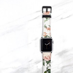 Op de afbeelding: Een wit Apple Watch bandje met een bloemenpatroon met roze rozen en groene bladeren.