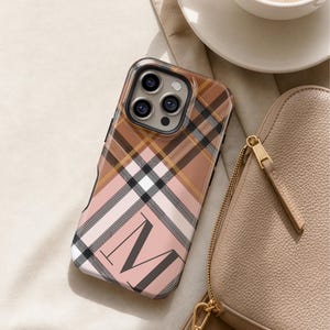 May include: A rectangular smartphone case featuring a plaid pattern in shades of tan, brown, black, and soft pink. The design includes a large, bold, black capital letter M printed on the lower portion of the case, with a camera cutout at the top.