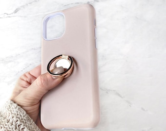 May include: A blush pink phone case with a rose gold ring holder. The ring holder has a clear center and a small crystal accent.