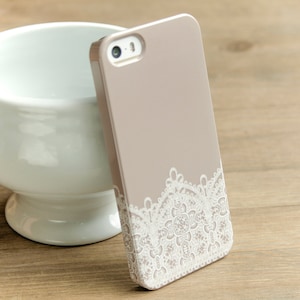 May include: A light brown phone case with a white lace design. The case has a camera hole in the top center.