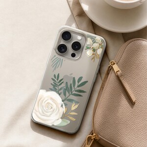 A smartphone with a floral design on its case, a cup of coffee, and a leather handbag are arranged on a beige surface.