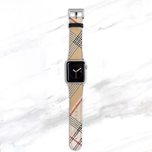 May include: A silver Apple Watch with a beige, black, and red plaid band.