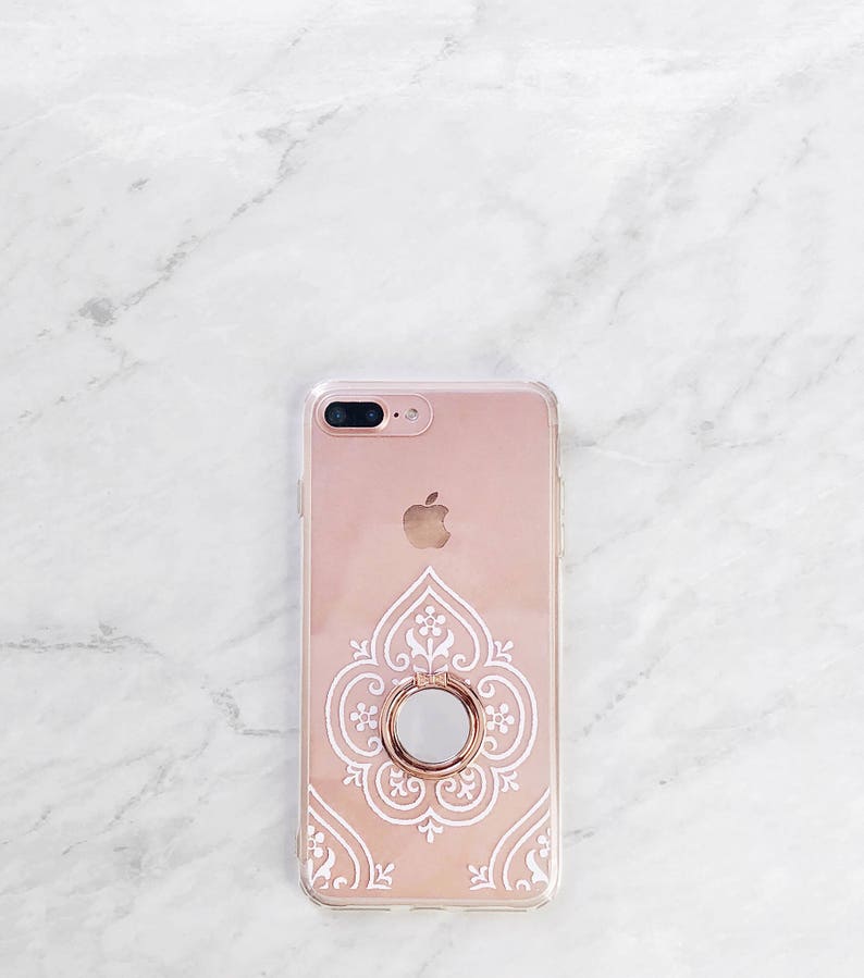 May include: A rose gold iPhone case with a white intricate design and a rose gold ring holder.