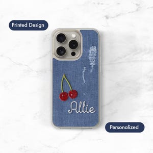 May include: A clear phone case with a blue denim effect. The case has an embroidered cherry design and the name "Allie" in white script. The words "Printed Design" and "Personalized" are also visible.