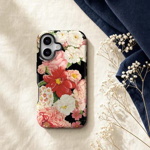 a phone case with a floral design, placed on a surface with a blue fabric and some white flowers.