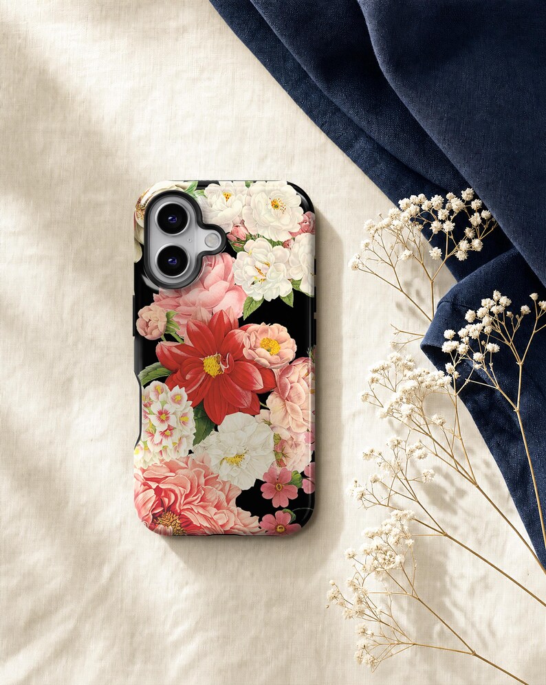 a phone case with a floral design, placed on a surface with a blue fabric and some white flowers.
