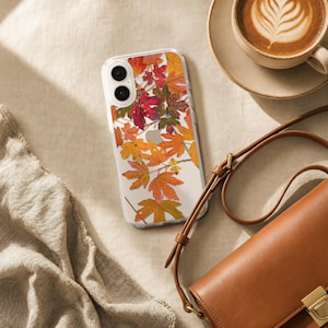 May include: A clear smartphone case featuring a printed pattern of vibrant autumn leaves in shades of red, orange, yellow, and green. The case has two circular camera cutouts on the upper left side and a central opening for the device logo.