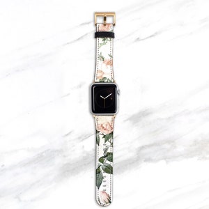 Op de afbeelding: Een witte Apple Watch met een band met bloemenprint. De band heeft roze rozen en groene bladeren op een witte achtergrond.