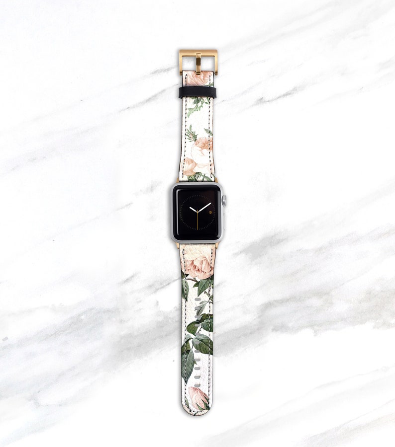 Op de afbeelding: Een witte Apple Watch met een band met bloemenprint. De band heeft roze rozen en groene bladeren op een witte achtergrond.