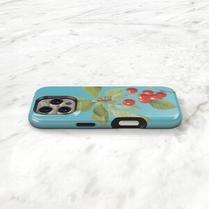 A turquoise phone case with a design of cherries and leaves on it, placed on a white marble surface.