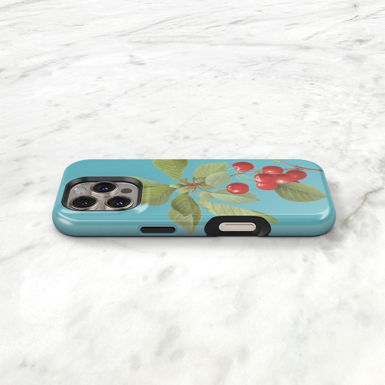 A turquoise phone case with a design of cherries and leaves on it, placed on a white marble surface.
