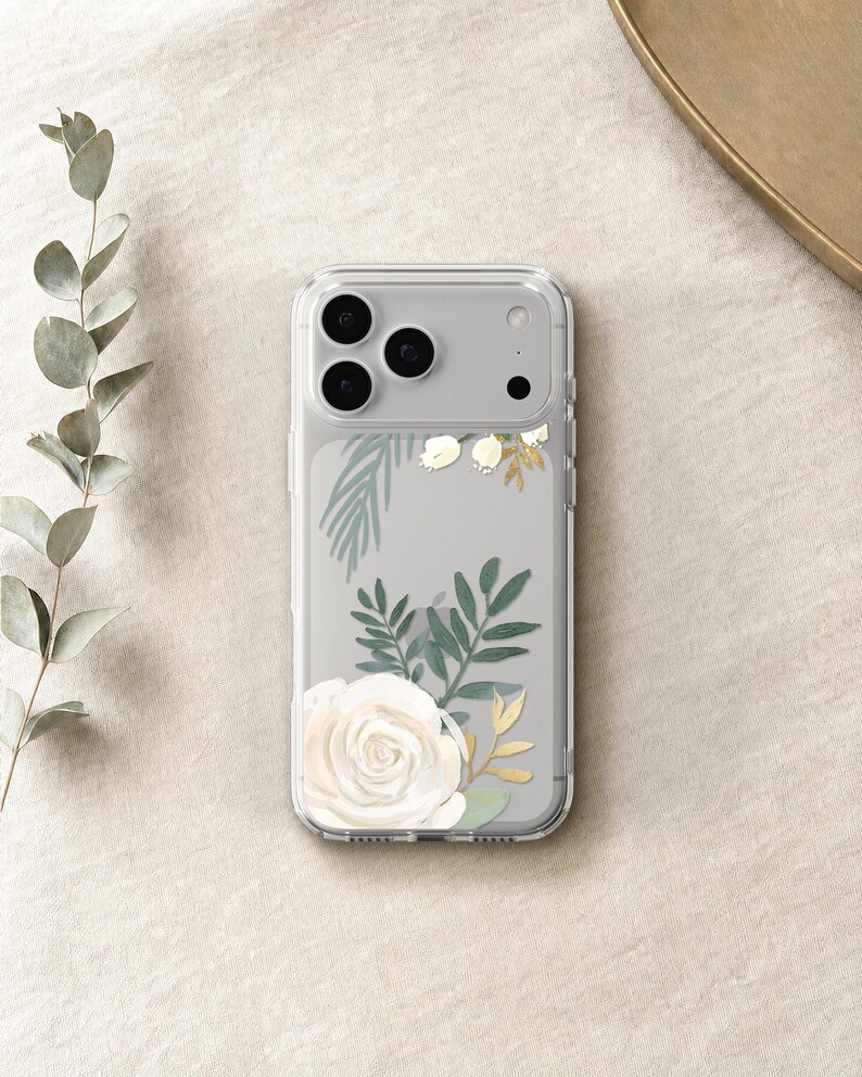A clear phone case with a floral design featuring a white rose and green leaves is placed on a beige surface.