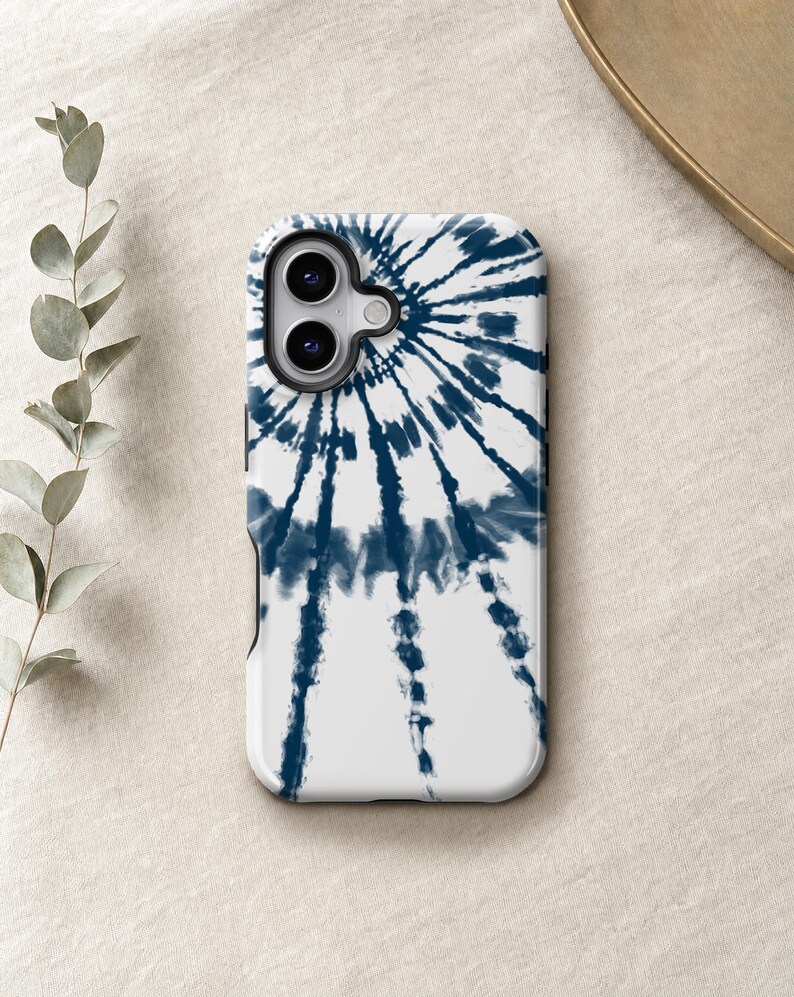 a white phone case with a tie-dye pattern on it, placed on a beige surface next to some greenery.