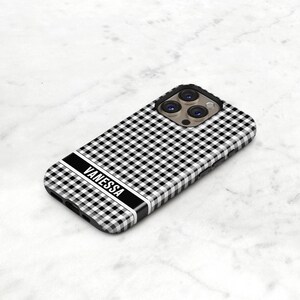 May include: A black and white gingham patterned phone case with the name "VANESSA" in white block letters. The case has a black border and a camera cutout. The phone case is on a white marble surface.