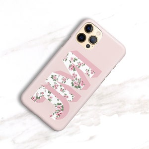 May include: A light pink phone case featuring the initials "JM" in a 3D design. The letters are filled with a floral pattern of pink roses and green leaves. The phone case has a smooth finish and a camera bump.