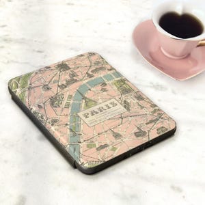 May include: A black electronic device case featuring a vintage map of Paris in pink, green, and blue. The case has the word "PARIS" printed on it. A pink heart-shaped saucer and a cup of coffee are in the background.