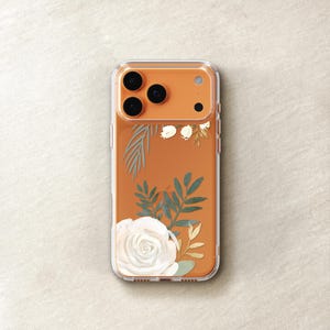 An orange-colored smartphone case with a floral design, including a white rose and green leaves, is shown on a light-colored surface.