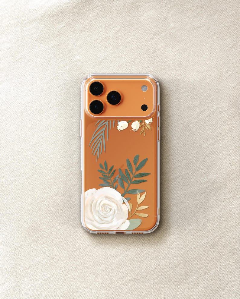 An orange-colored smartphone case with a floral design, including a white rose and green leaves, is shown on a light-colored surface.