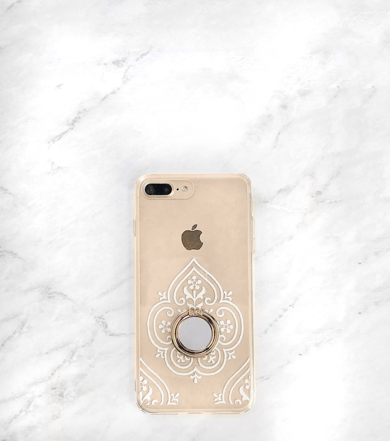 May include: A gold iPhone case with a white intricate design and a gold ring holder.