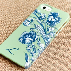 May include: A mint green iPhone case with a blue and white floral design and the letter "L" printed on the back.