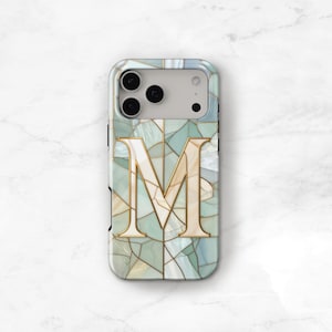 May include: A phone case with a mosaic design in shades of blue, green, and gold. The letter "M" is prominently displayed in gold, centered on the case. The case has a glossy finish and a modern aesthetic.