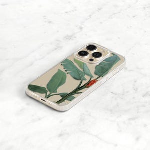 A clear phone case with a tropical leaf design. The case has a clear background with green leaves and a red flower. The case is designed for an iphone with a triple lens camera.
