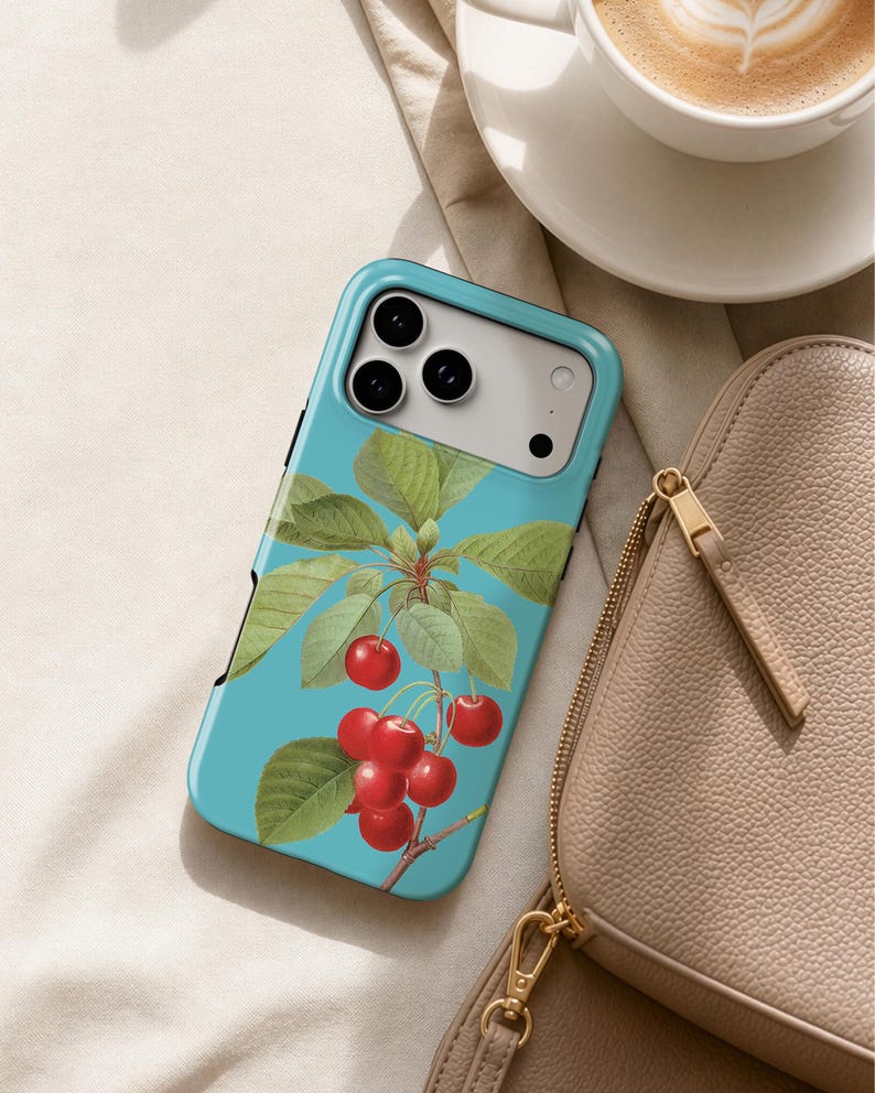 A teal-colored phone case with a cherry tree design, a white coffee cup, and a tan purse are arranged on a beige surface.