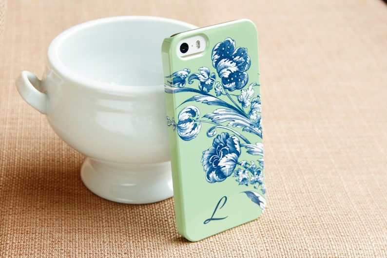 May include: A mint green iPhone case with a blue and white floral design and the letter "L" in the lower right corner.