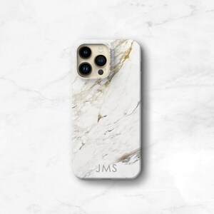 May include: White iPhone case with a marble pattern and gold accents. The case has a cutout for the camera lens and the text "JMS" is printed on the back.