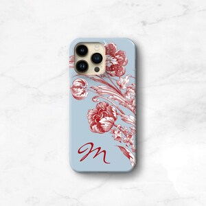 May include: A light blue smartphone case featuring a red floral toile pattern and a red cursive letter M. The design includes detailed botanical illustrations of flowers and leaves, with a cutout for the triple camera lens system on the back.