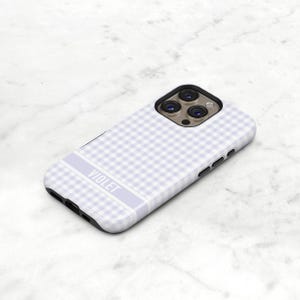 May include: A light purple phone case with a gingham pattern. The case has a rectangular design with rounded corners and a black border. The word "VIOLET" is printed in white on a light purple stripe.