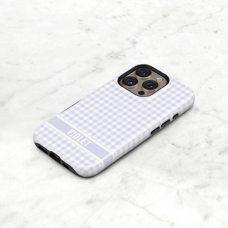 May include: A light purple phone case with a gingham pattern. The case has a rectangular design with rounded corners and a black border. The word "VIOLET" is printed in white on a light purple stripe.
