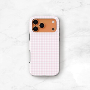 May include: A pink and white gingham pattern phone case. The case has a protective bumper and covers the back and sides of the phone. The camera lenses are visible at the top of the case.