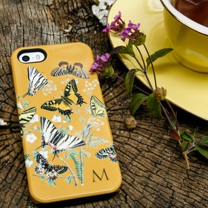 May include: A yellow phone case with a butterfly design. The case has a black camera lens and a white letter "M" in the bottom right corner.