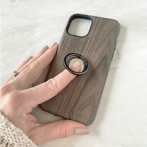 May include: A dark wood phone case with a black ring holder. The ring holder has a mirror on the front.