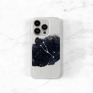May include: Clear phone case featuring a dark blue and black watercolor design with white star-like accents. A white constellation outline is visible. The phone case is designed to fit a smartphone.