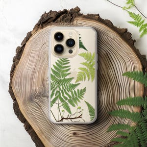 May include: A clear smartphone case featuring a botanical print of green fern fronds and small brown stems. The design is layered over a light cream background, showcasing the natural details of the leaves and the visible Apple logo.
