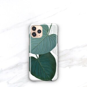 May include: A white phone case with a green leaf design. The case has a camera lens cutout and a gold trim.
