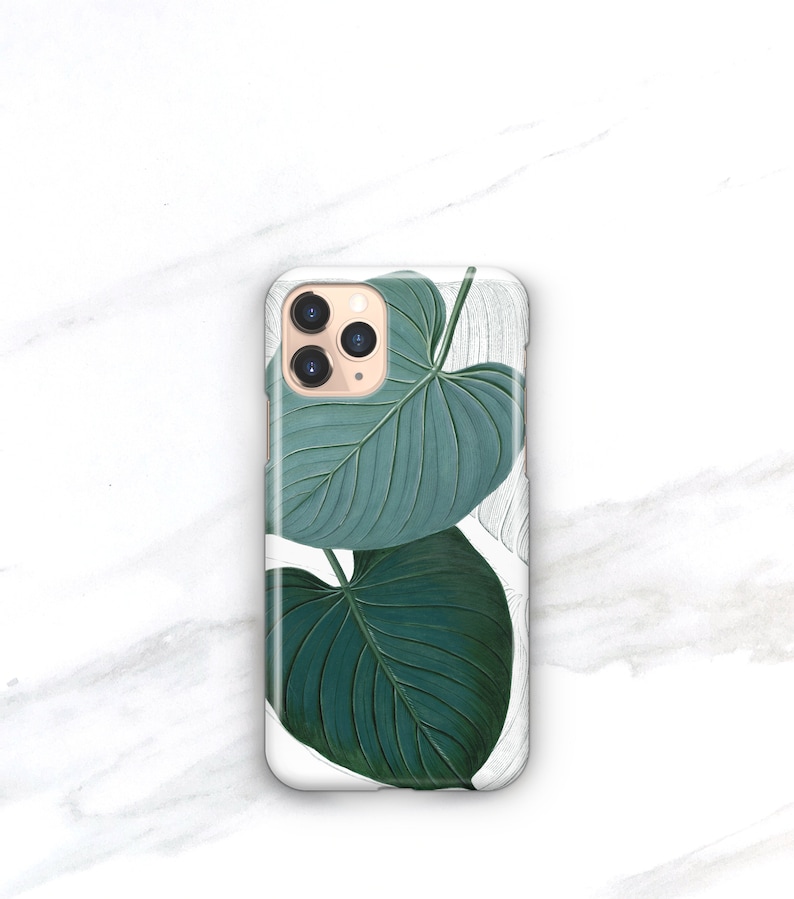 May include: A white phone case with a green leaf design. The case has a camera lens cutout and a gold trim.