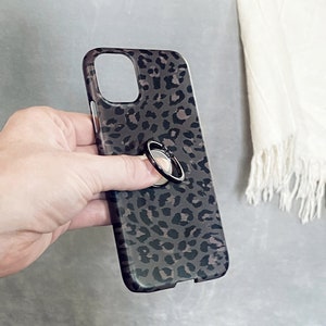 May include: A black phone case with a leopard print design. A black ring holder is attached to the back of the case.