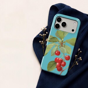 A smartphone case with a blue and green design featuring a branch with red cherries and green leaves, placed on a blue cloth.