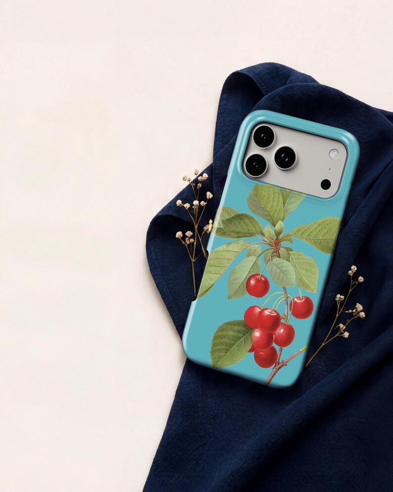 A smartphone case with a blue and green design featuring a branch with red cherries and green leaves, placed on a blue cloth.