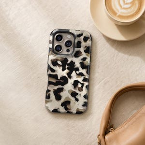 May include: A rectangular smartphone case featuring a high-contrast leopard print pattern in shades of black, cream, and translucent taupe. The case has a dedicated cutout for a triple-lens camera system and a flash, with a smooth, glossy finish.