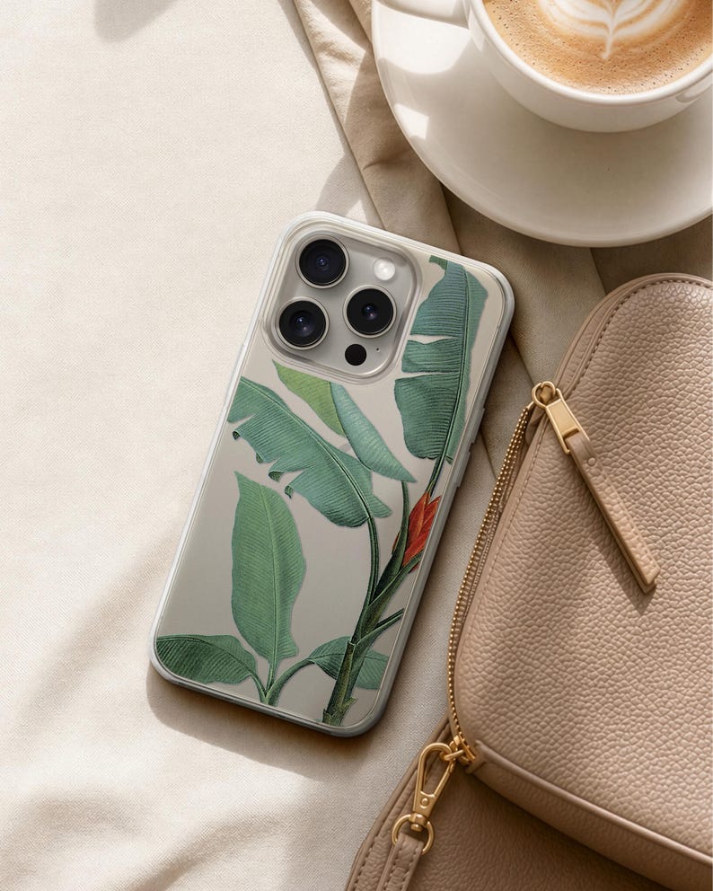 A smartphone with a leafy green and red plant design case, a beige purse, and a cup of coffee are arranged on a beige surface.