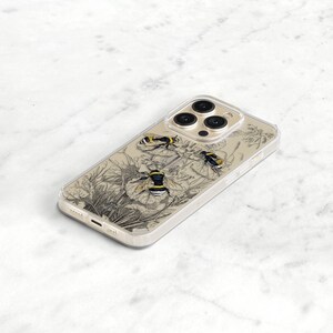 May include: A clear phone case with a black and white illustration of bees and flowers. The case is designed for an iPhone with a triple camera lens.